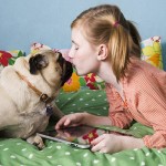 Girl holding tablet PC while kissing dog